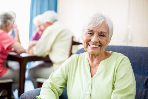 senior woman seated looking at viewer with other aged people in the backgroubd