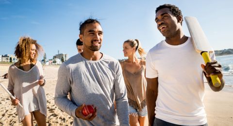 Group of young people from diverse ethnicities walking along an Australian beach with a cricket bat 